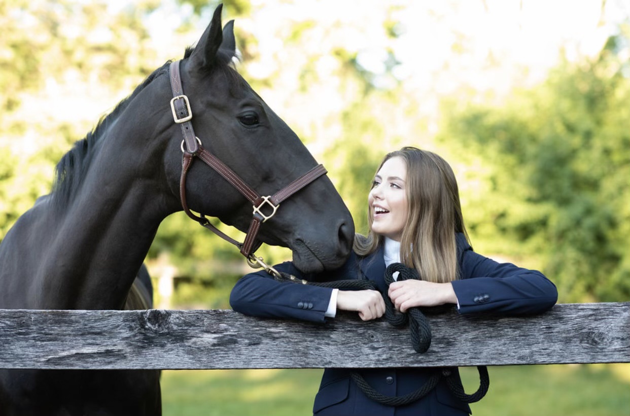 Blond woman in riding uniform smiling at a dark Thoroughbred horse