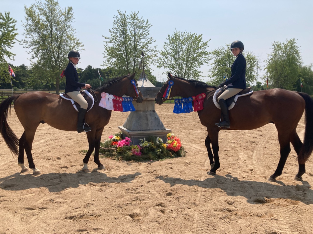Two riders in uniform posing on their horses with countless award ribbons